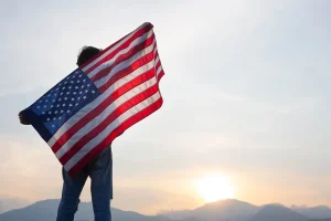 a man with his fully sized US flag starring at the sunset